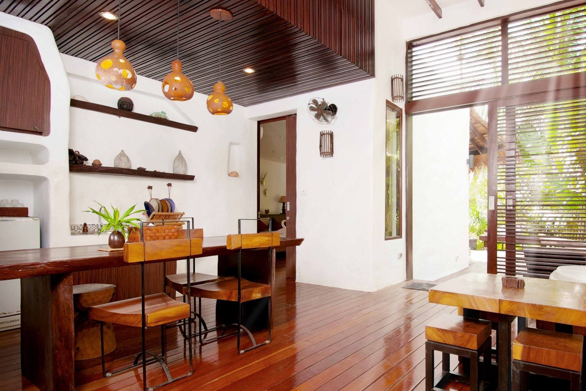 A modern interior with a wooden dining table and bar area, pendant lights, and a large window with blinds.