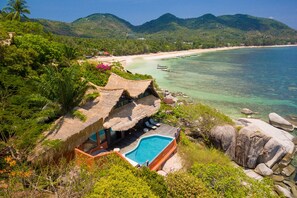 A thatched-roof structure with a pool, surrounded by lush greenery and overlooking a beach with boats. - Koh Tao Cabana Resort (Koh Tao)