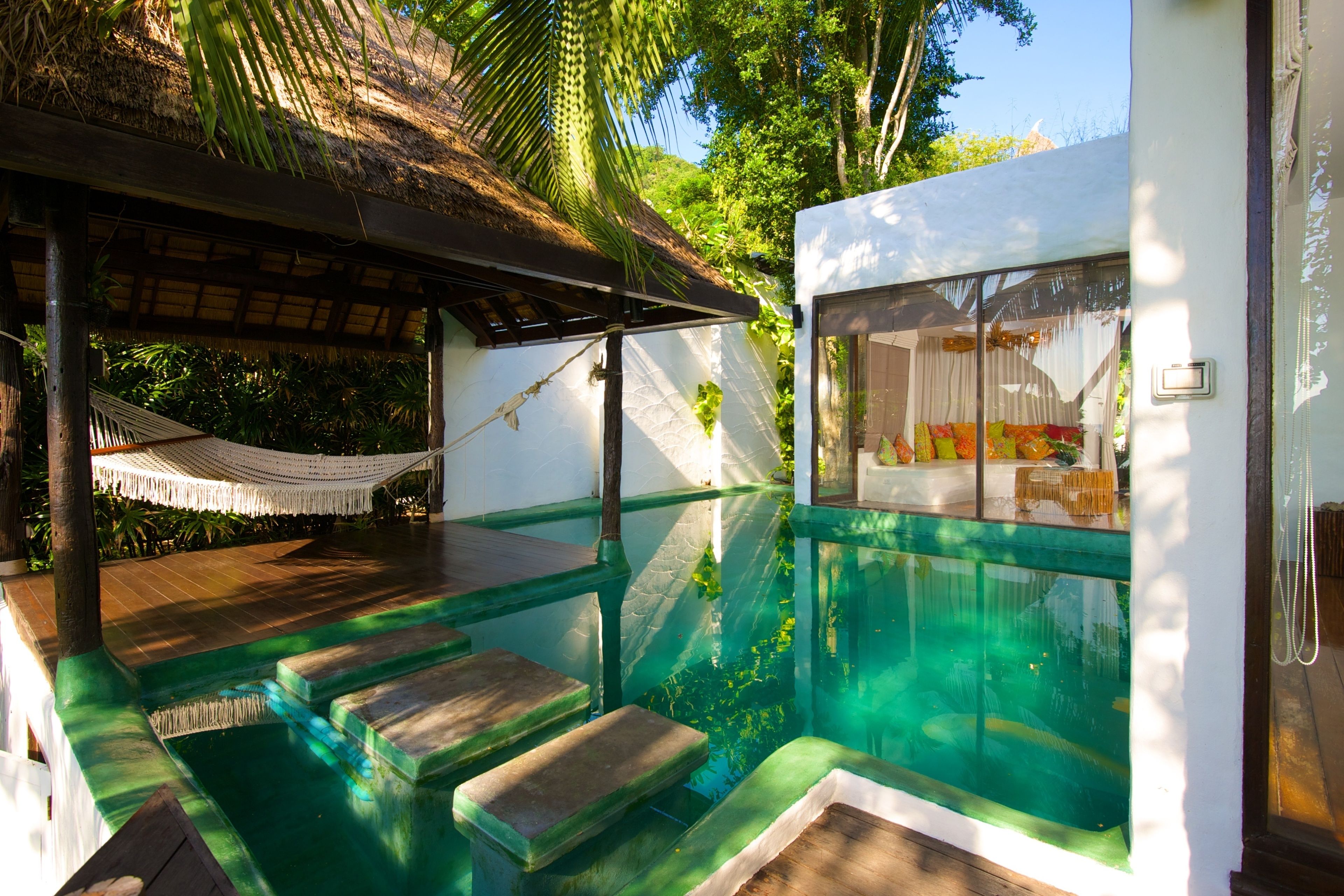 A pool area with steps leading into the water, a hammock, and a view of the surrounding greenery.