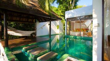 A pool area with steps leading into the water, a hammock, and a view of the surrounding greenery.