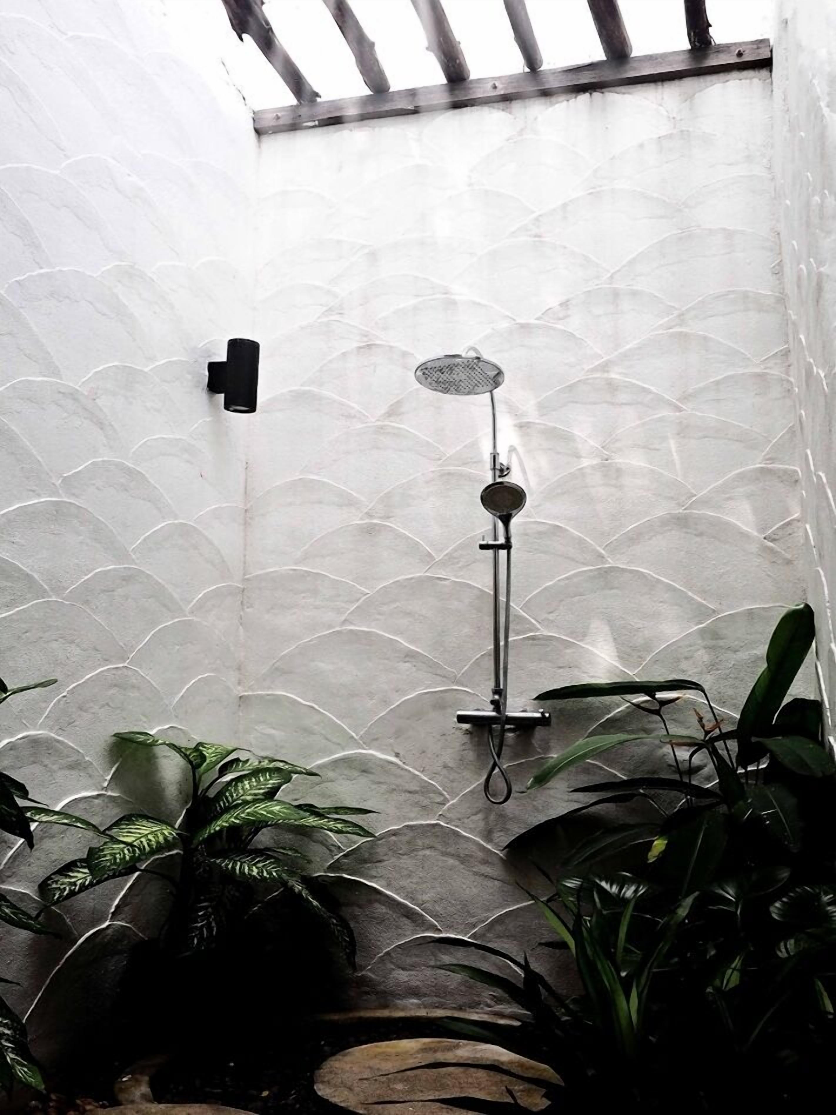 A shower area with a textured wall, a handheld showerhead, and a wall-mounted control.