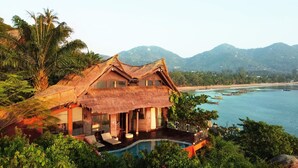 A house with a thatched roof, a swimming pool, and a view of the sea and mountains.