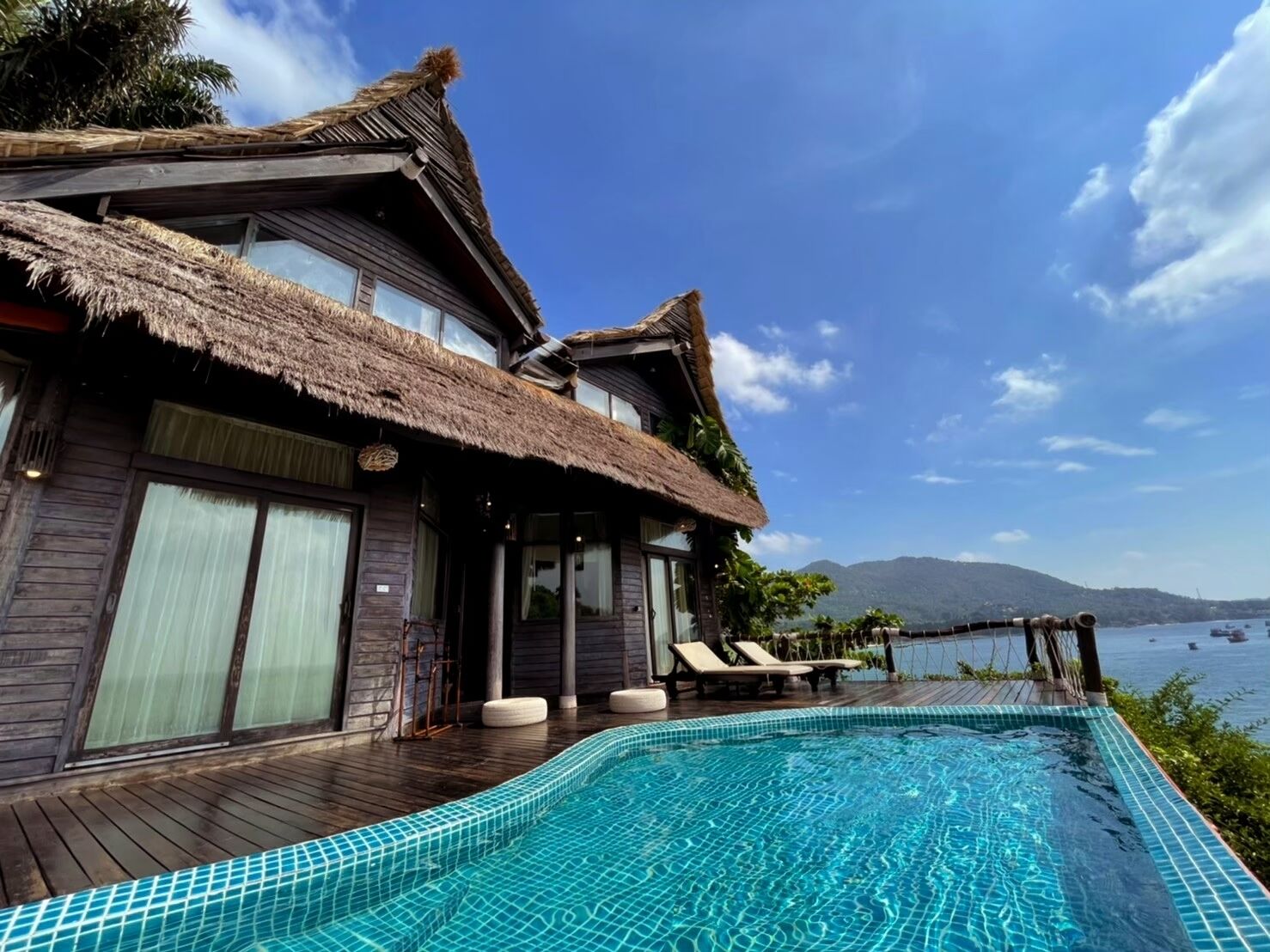 Ein zweistöckiges Haus mit einem Strohdach, einem Swimmingpool und Meerblick.