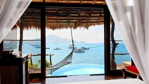 A bedroom with a view of boats on the water, a hammock, and an open book with flowers.