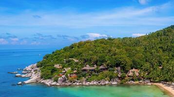 Un resort playero tropical con cabañas de techo de paja, una costa rocosa y aguas turquesas cristalinas.