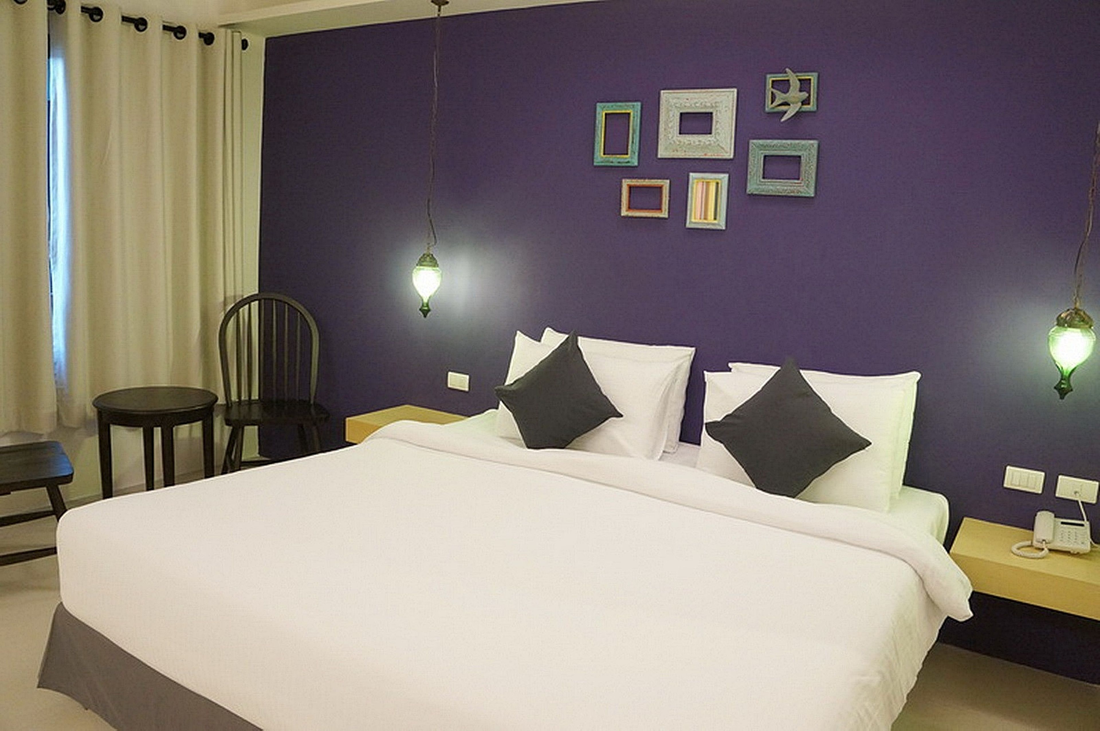 A hotel room with a large bed, a chair, a bedside table with a phone, and wall-mounted picture frames.