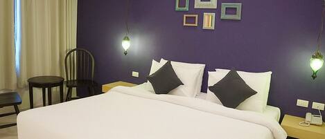 Habitación de hotel con una cama grande, una silla, una mesita de noche con teléfono y marcos de cuadros en la pared.