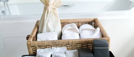 Une salle de bain avec un panier en osier contenant des serviettes, un sac à cordon et des bonnets de douche.