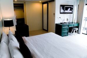 Una habitación de hotel con cama, escritorio, televisor y ventana con cortinas.
