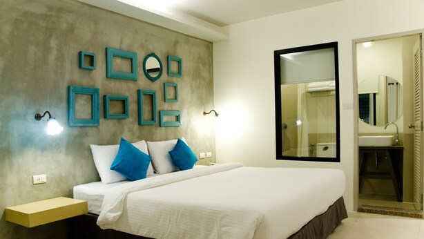 Une chambre moderne avec un grand lit, des tables de chevet, un miroir fixé au mur et une salle de bain visible à travers une porte ouverte.