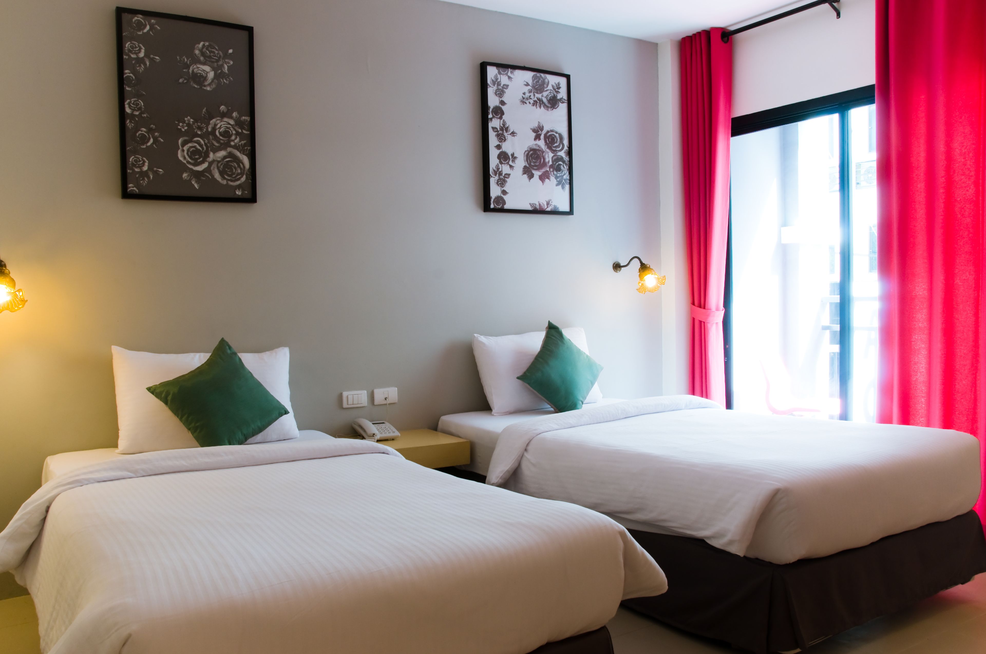 Ein Hotelzimmer mit zwei Betten, jeweils mit weißer Bettwäsche und grünen Kissen, einem Nachttisch mit Lampe sowie zwei gerahmten Blumenbildern an der Wand.