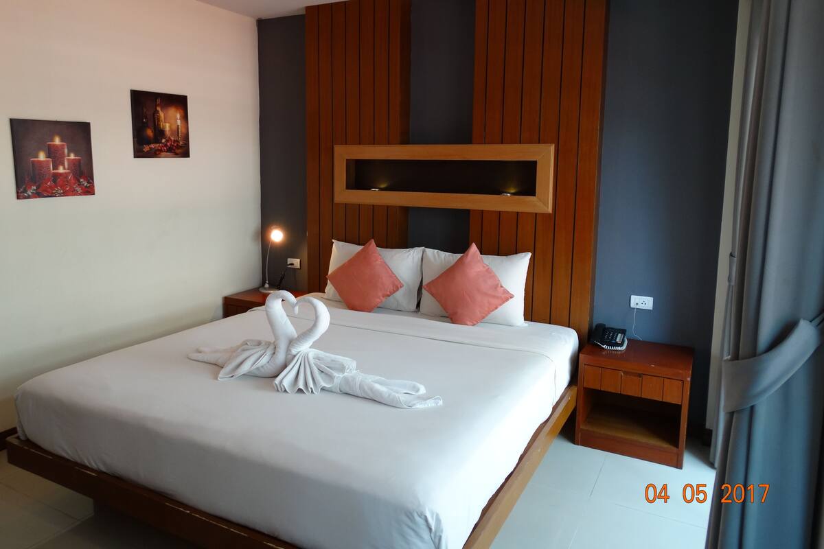 A hotel room with a large bed, wooden headboard, two nightstands, a wall-mounted TV, and a telephone.