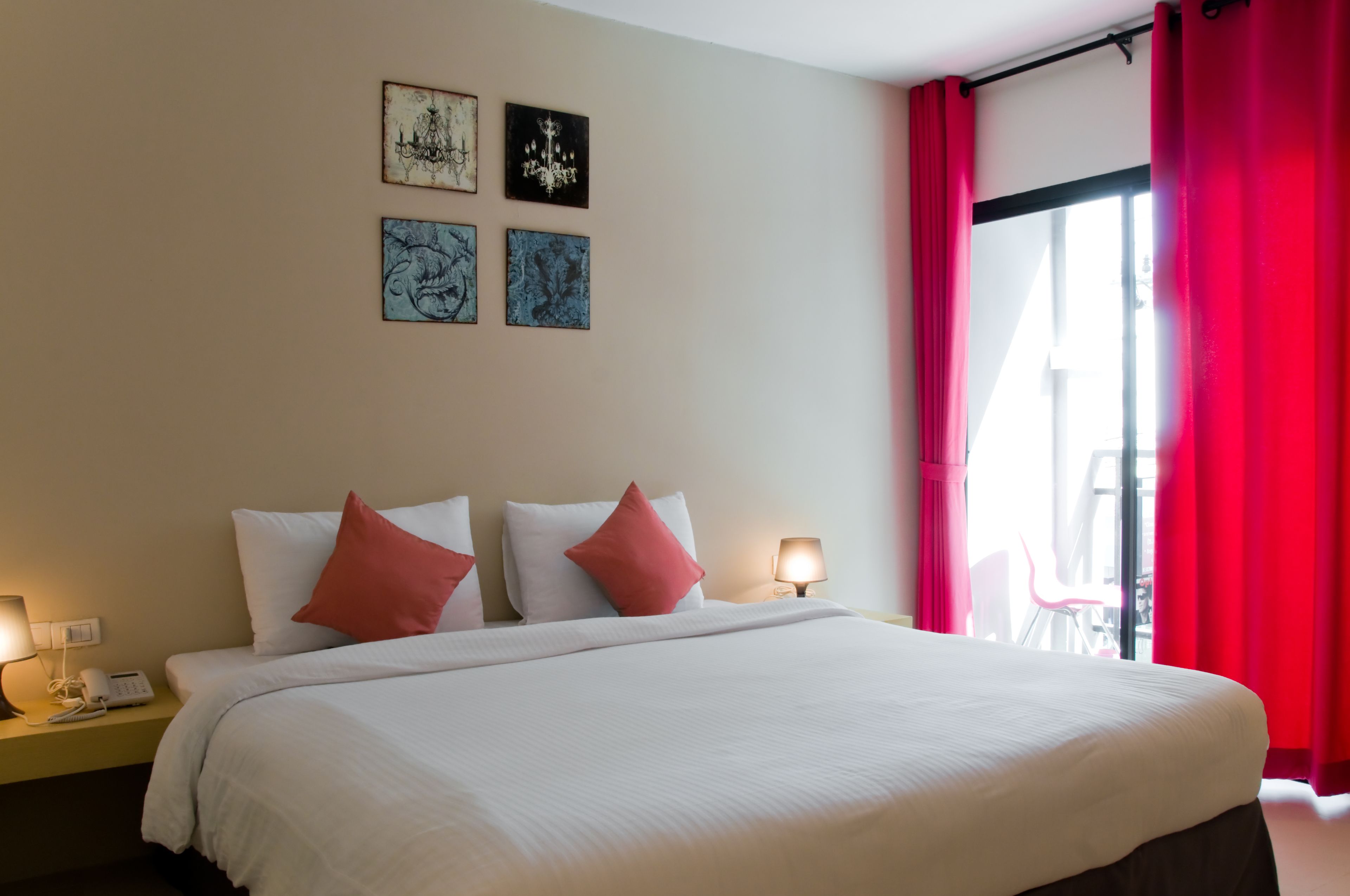 A hotel room with a large bed, two bedside lamps, and a window with red curtains.