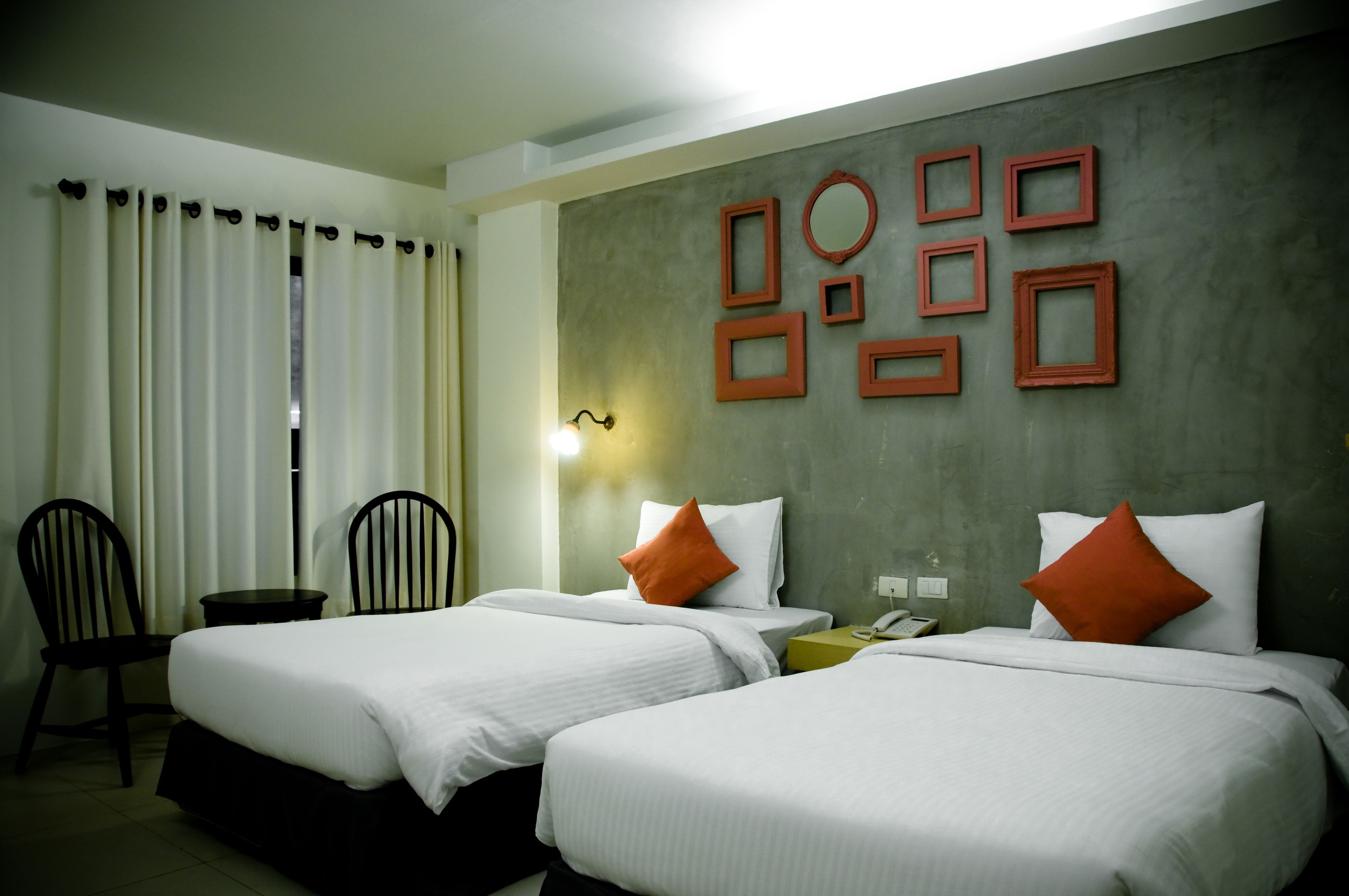 A hotel room with two beds, a desk, chairs, and a wall with framed pictures.