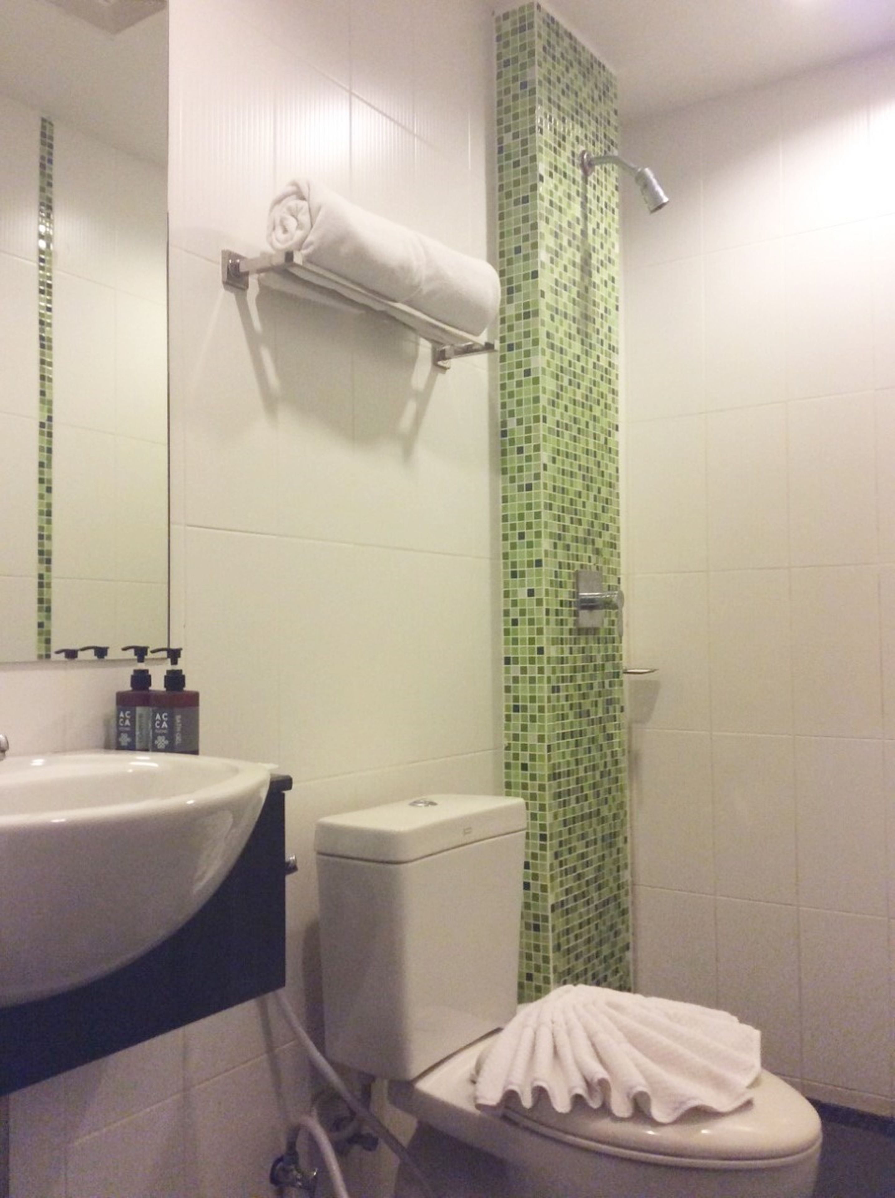 A bathroom with a white sink, a toilet, and a shower with green mosaic tiles.