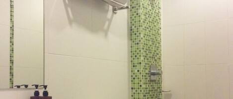 A bathroom with a white sink, a toilet, and a shower with green mosaic tiles.