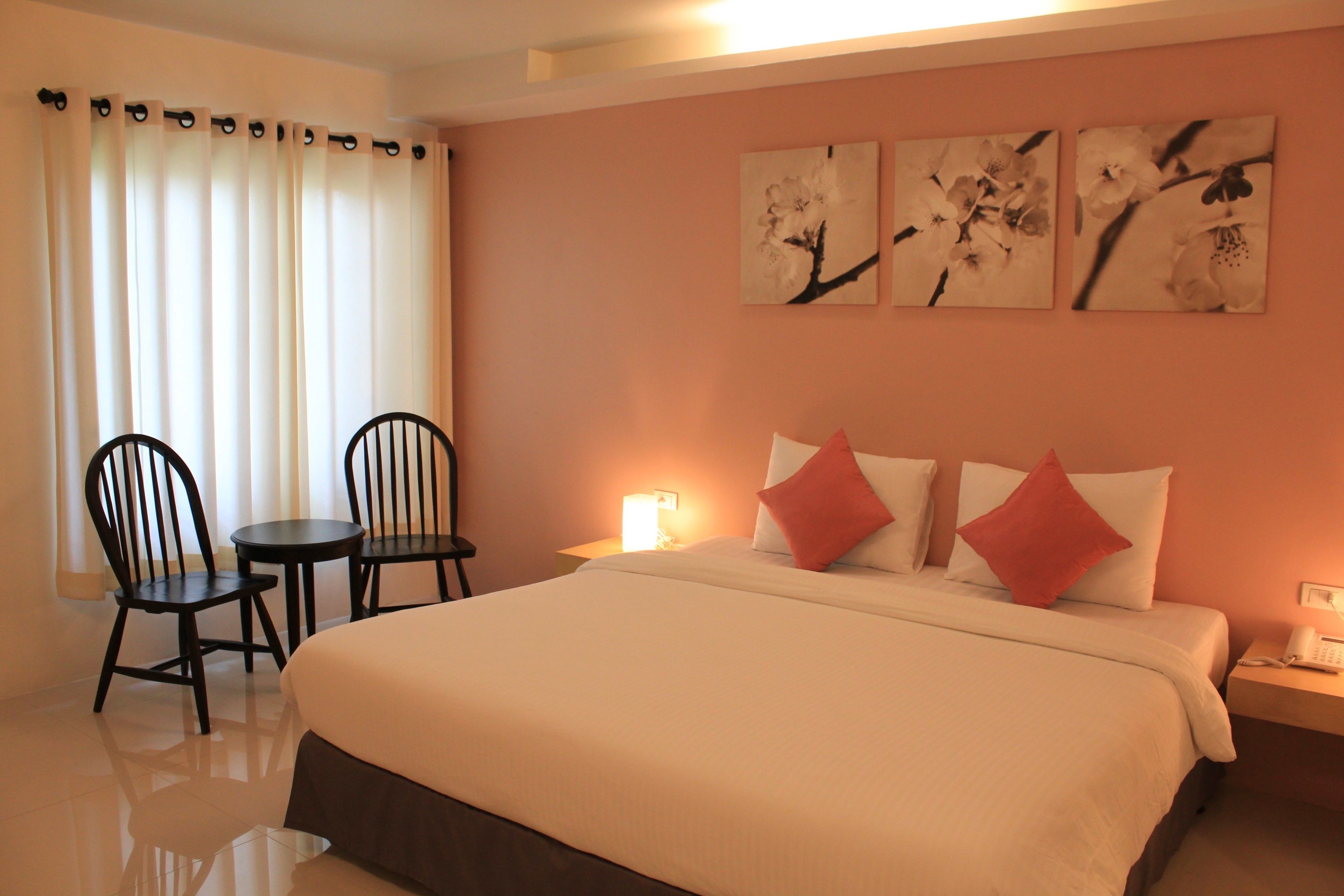 A hotel room with a bed, two chairs, a small table, and a nightstand with a phone.