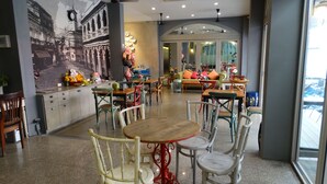 Un café spacieux orné d’une fresque représentant une scène de rue, avec de nombreuses tables et chaises, et offrant une vue sur la rue grâce à de grandes fenêtres.