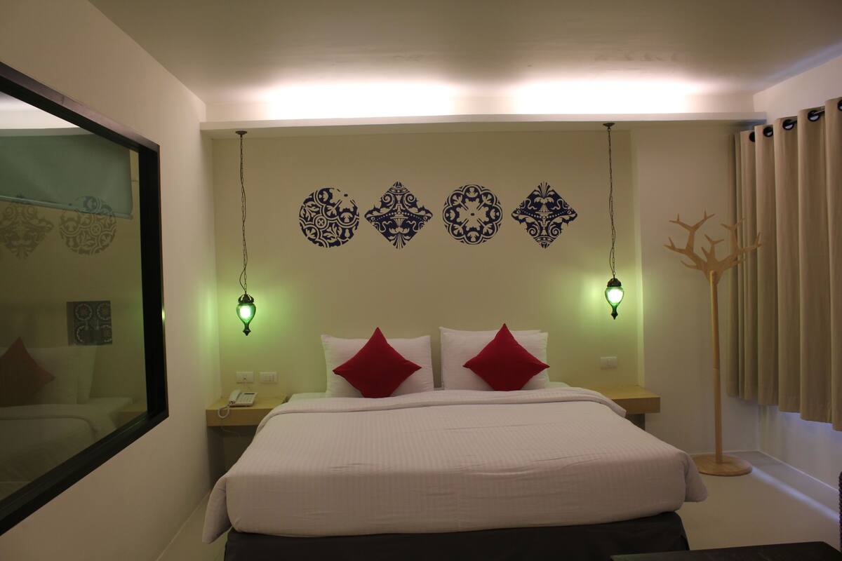 A hotel room with a large bed, two red pillows, a bedside table with a phone, and decorative wall art.