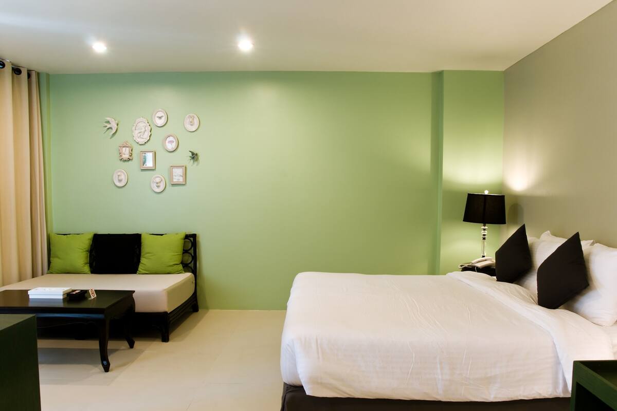 A hotel room with a bed, a sofa, a table, and a lamp.