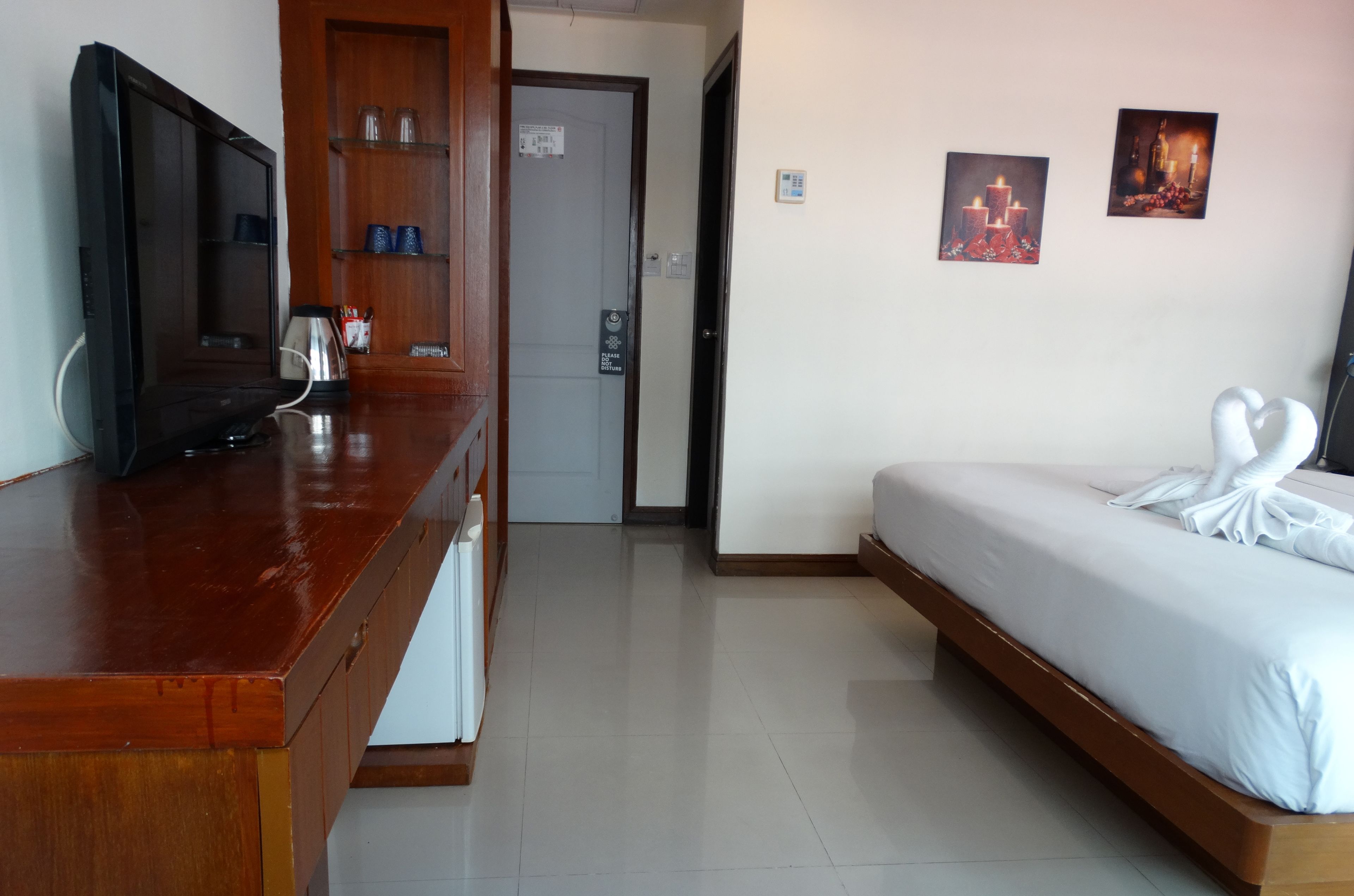 A hotel room with a wooden desk, a bed with white linens, and two framed pictures on the wall.