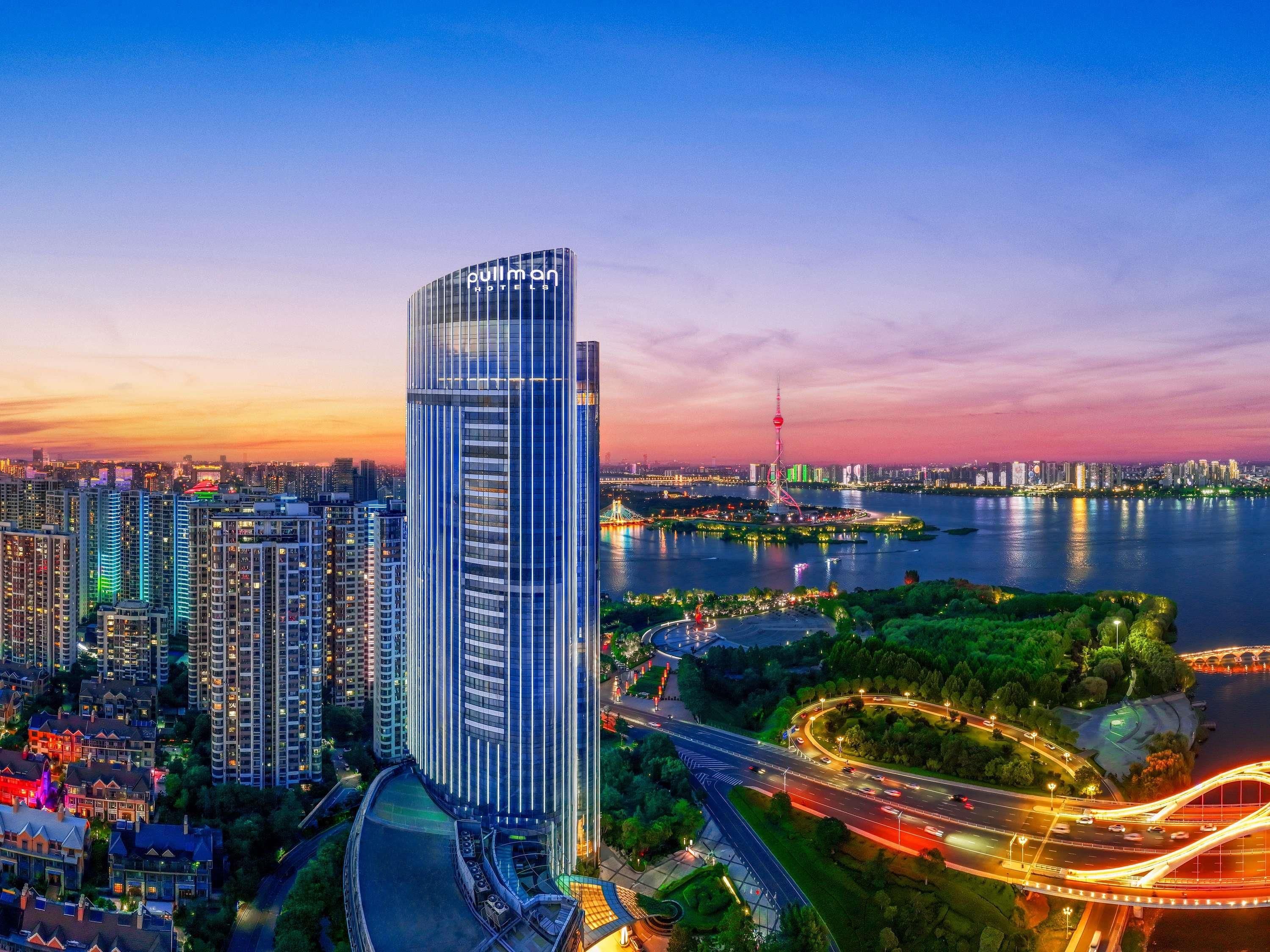 A high-rise building with a modern design, surrounded by a river and a bridge, with a cityscape in the background.