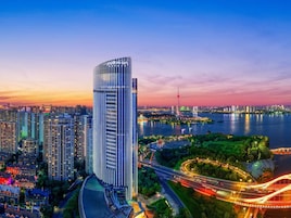 A high-rise building with a modern design, surrounded by a river and a bridge, with a cityscape in the background.