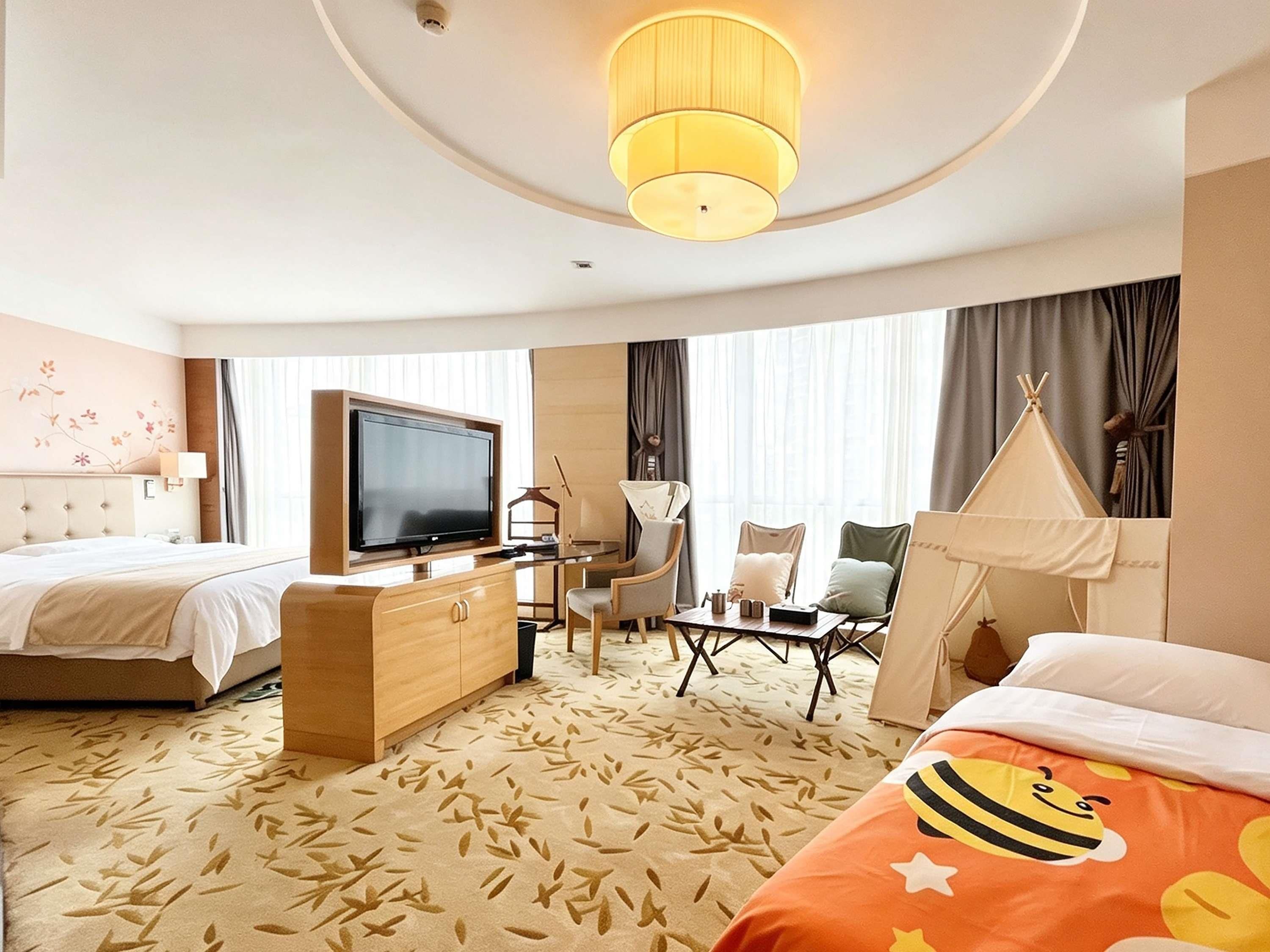 Een hotelkamer met een bed, een bureau, een televisie, een stoel, een klein tafeltje, een lamp en een tentachtige constructie.