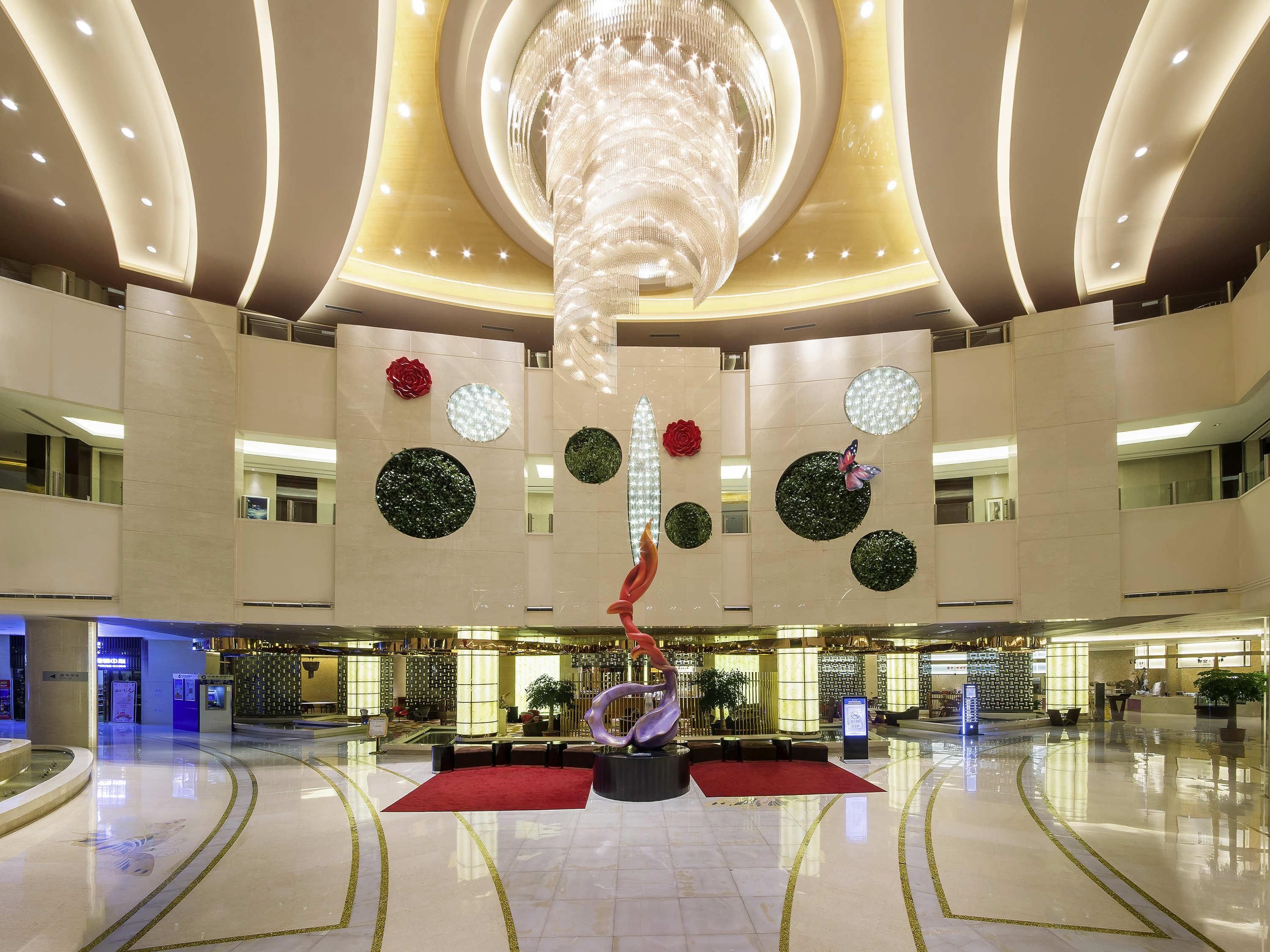 A spacious lobby with a central red carpet, a large chandelier, and decorative wall art.