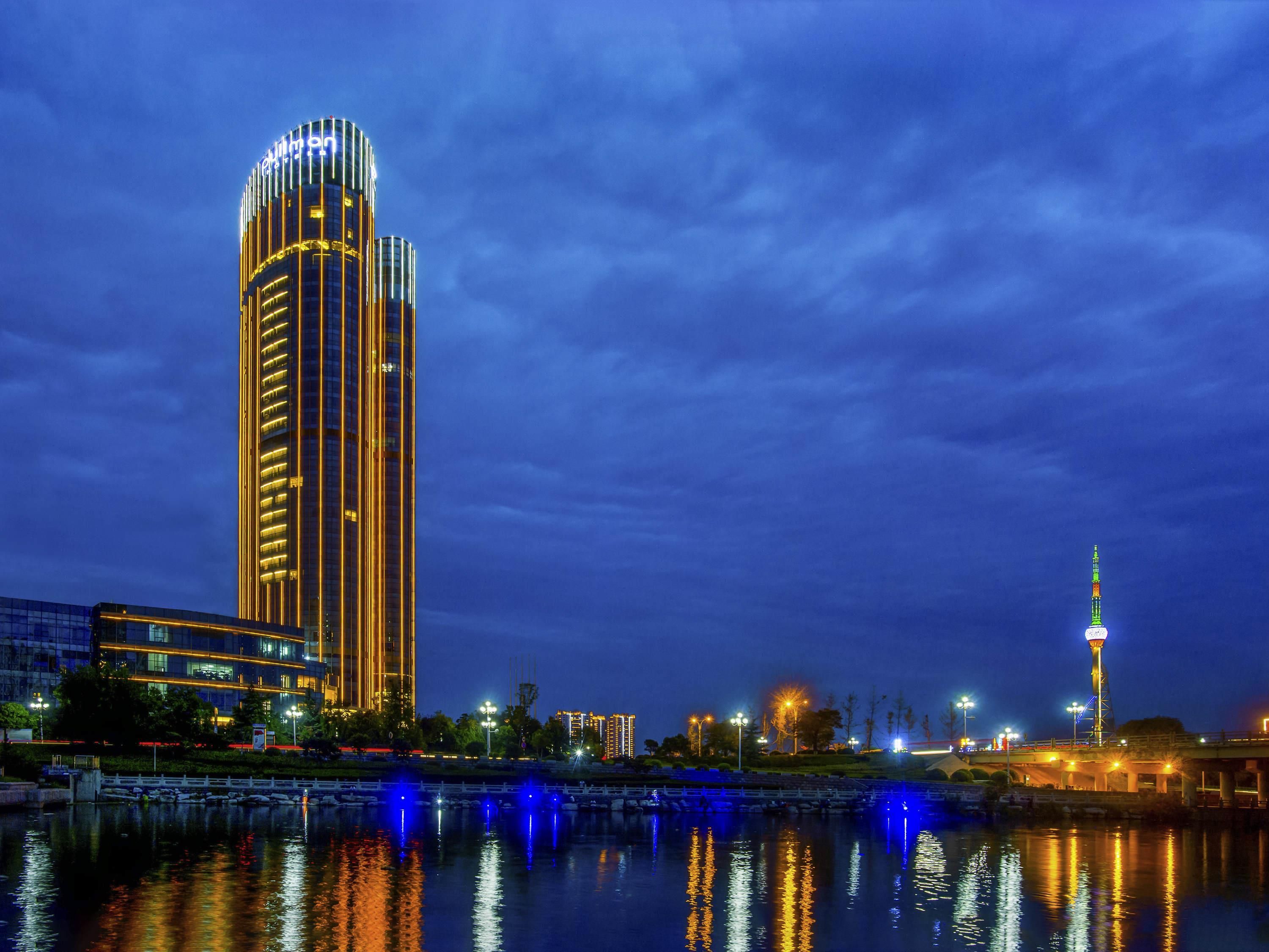 A high-rise hotel with a modern design, located near a body of water with reflections of lights.