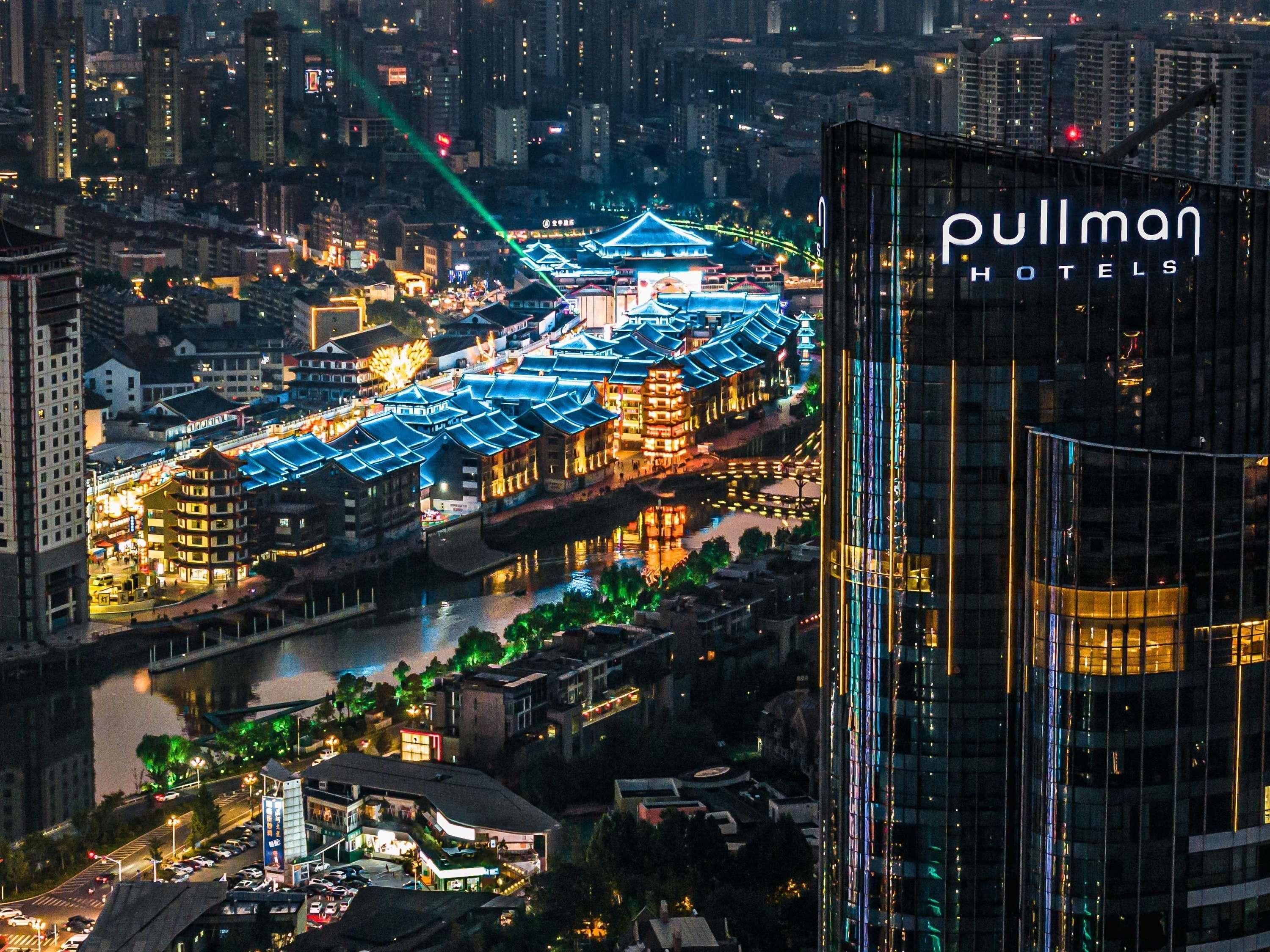 A hotel with a modern glass facade, traditional Chinese architecture, and a river view.