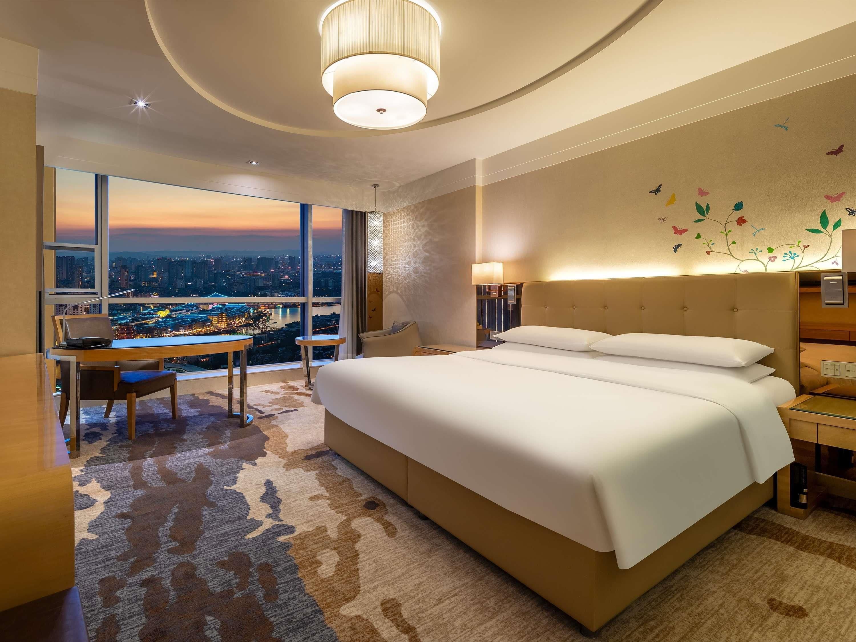 Una camera d'albergo con un letto grande, una scrivania e vista sulla città al tramonto.