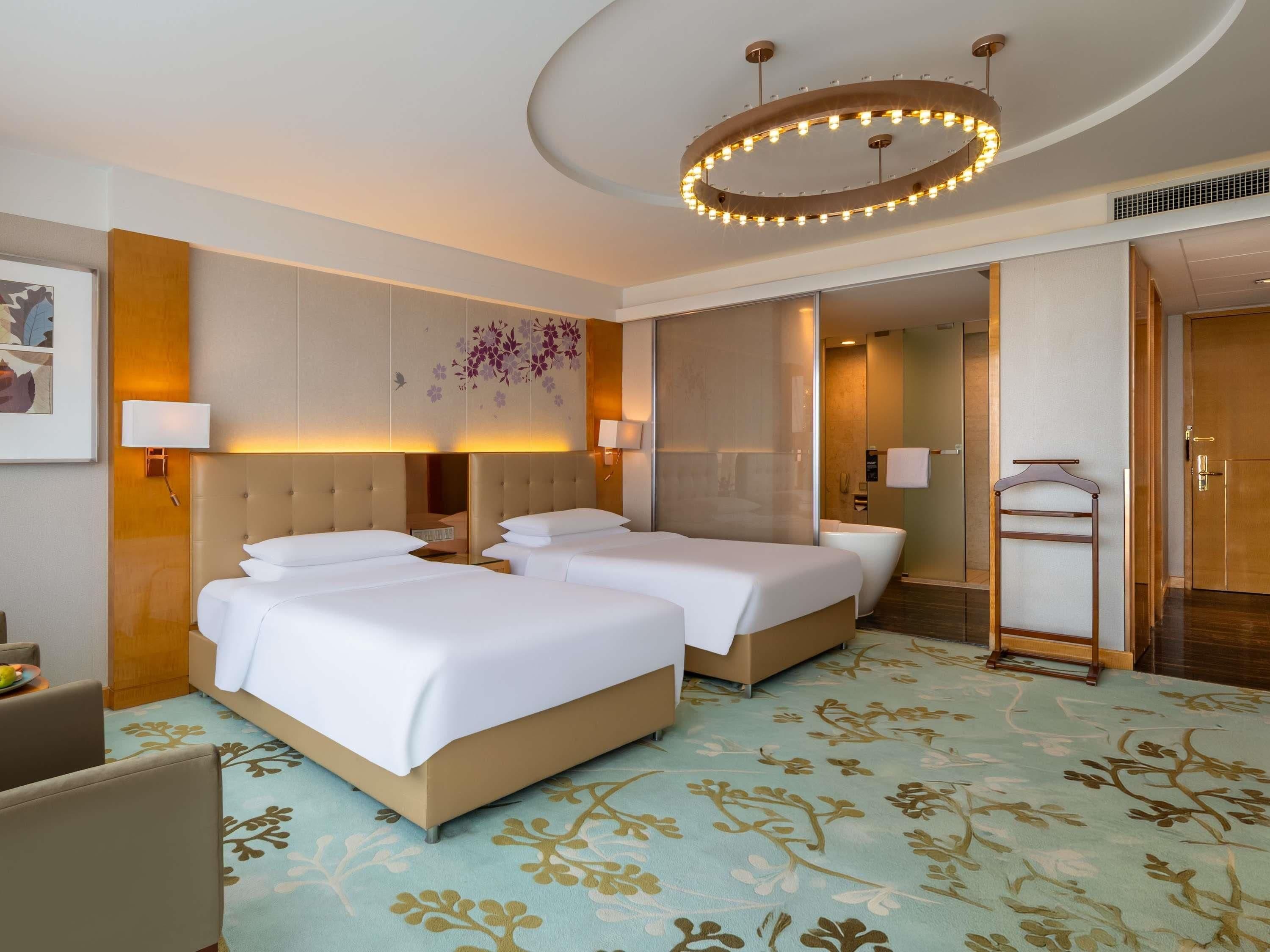 A hotel room with two beds, a large mirror, a chandelier, and a patterned carpet.