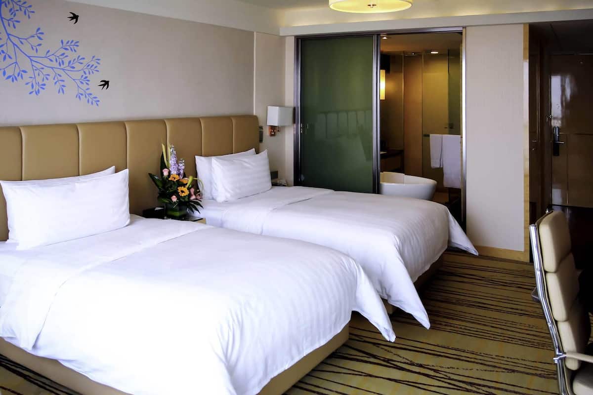 Ett hotellrum med två sängar, en soffa, en fåtölj, ett skrivbord och en grön dörr.