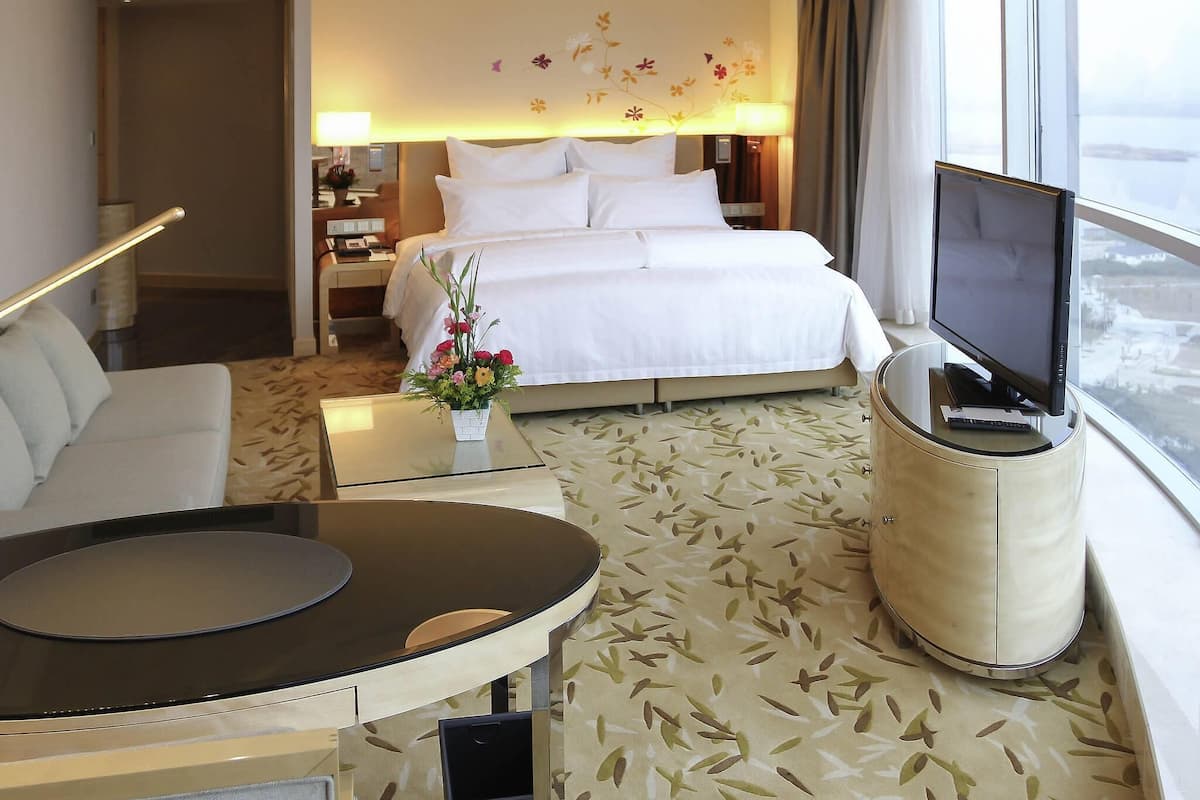 Ett hotellrum med en säng, en tv, en soffa, ett soffbord och ett litet bord med en blomsteruppsättning.