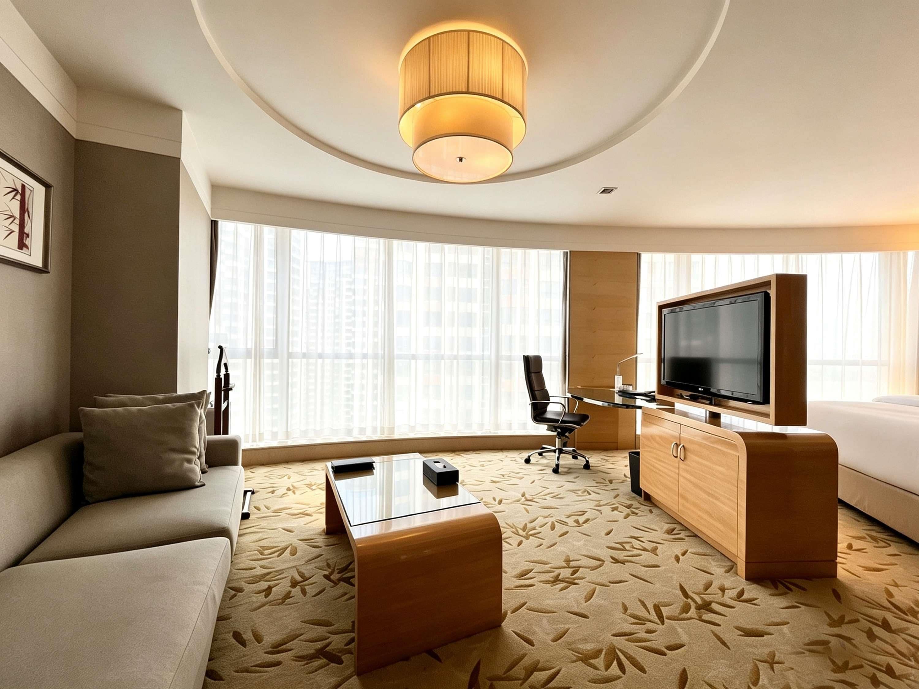 A hotel room with a sofa, a coffee table, a TV, and a large window with blinds.