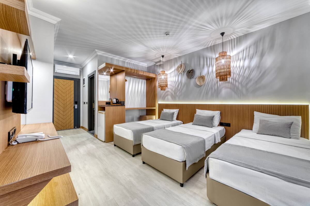 A hotel room with three beds, a desk, a TV, and a mirror.