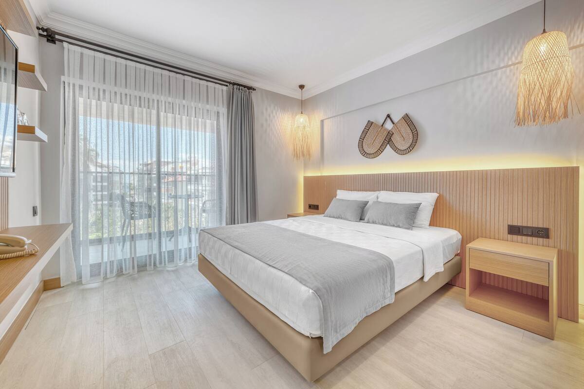 A modern bedroom with a large bed, a bedside table, a nightstand, and a view of the outdoors.