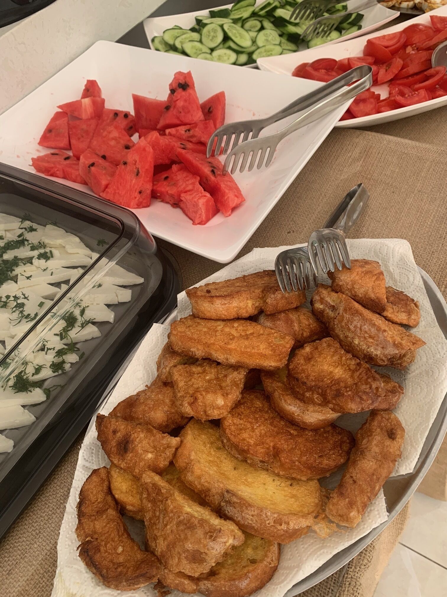 Un tavolo da buffet con diversi cibi, tra cui anguria a fette, cetrioli e fritti.