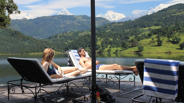 Une terrasse au bord du lac, dotée de chaises longues et d’une table, offrant une vue sur le lac et les montagnes.