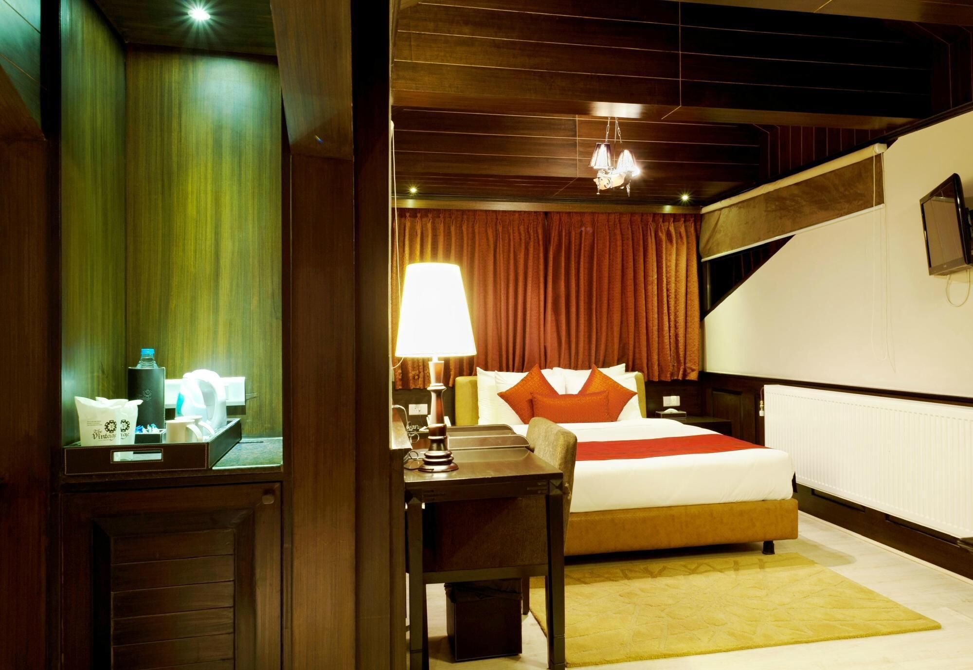 A hotel room with a bed, a desk with a lamp, a chair, and a small table with a bottle and tissues.