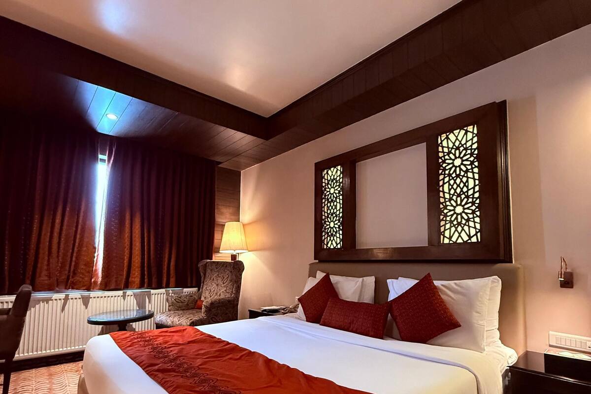 A hotel room with a large bed, a chair, a small table, and a window with curtains.