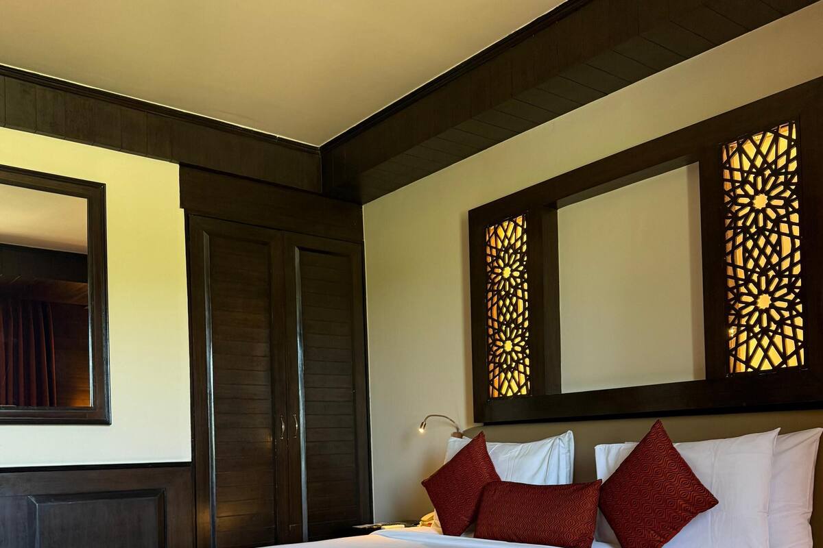 A hotel room with a large bed, dark wooden headboard, and a decorative wall panel.