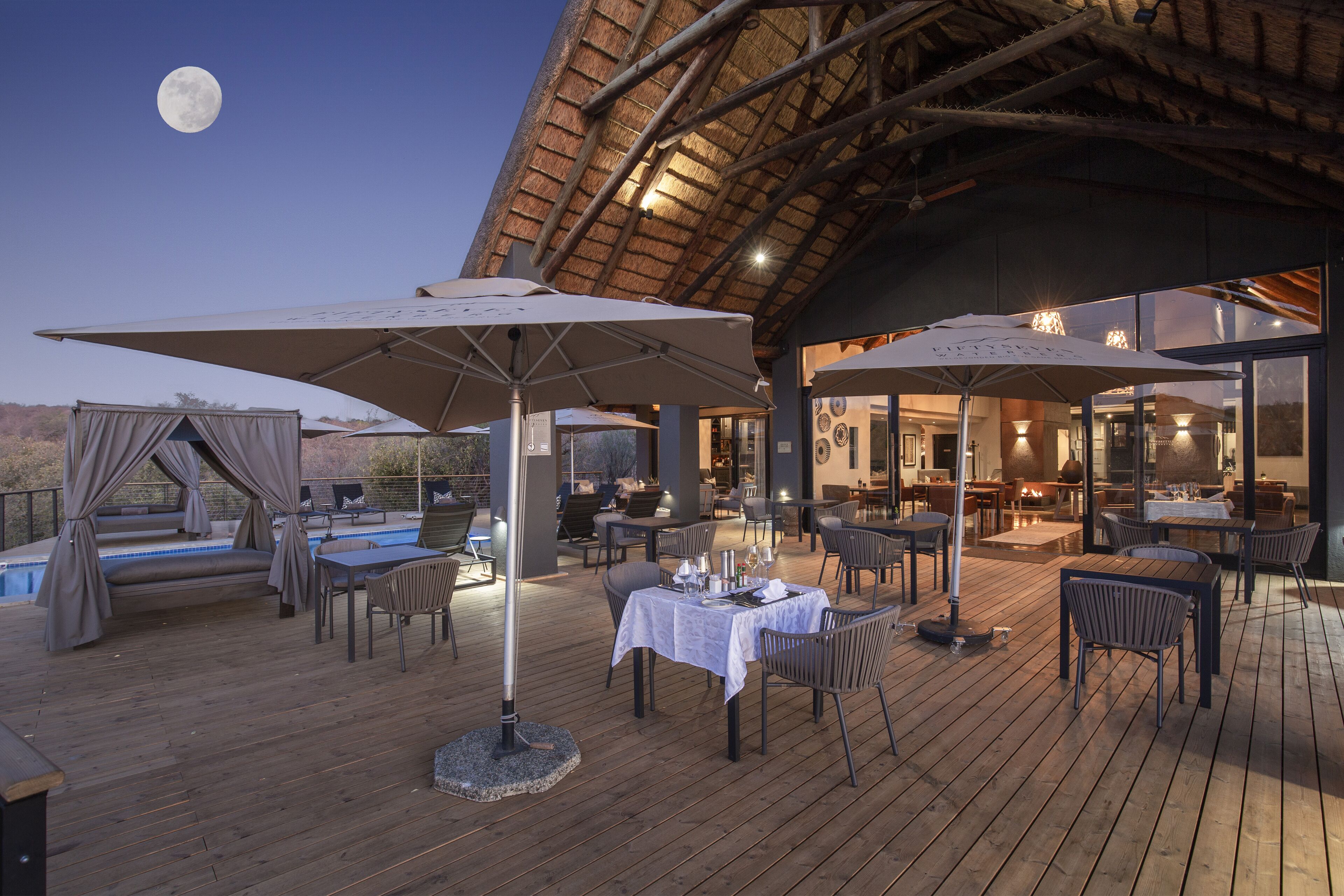 Un espace extérieur aménagé pour les repas, avec des tables et des chaises, une piscine et une structure dotée d’un toit de chaume.
