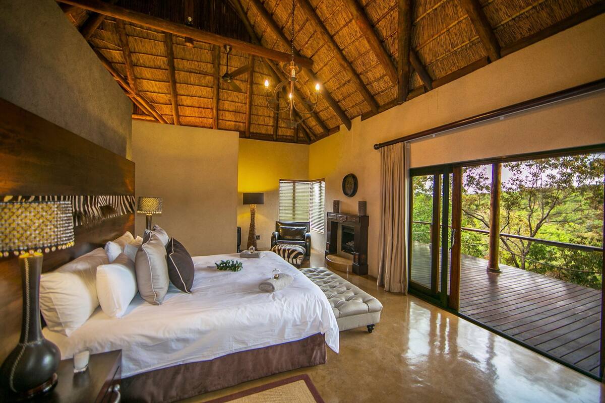Une chambre à coucher comprenant un lit, des lampes de chevet, une table de chevet, une chaise, une cheminée et un balcon avec vue.