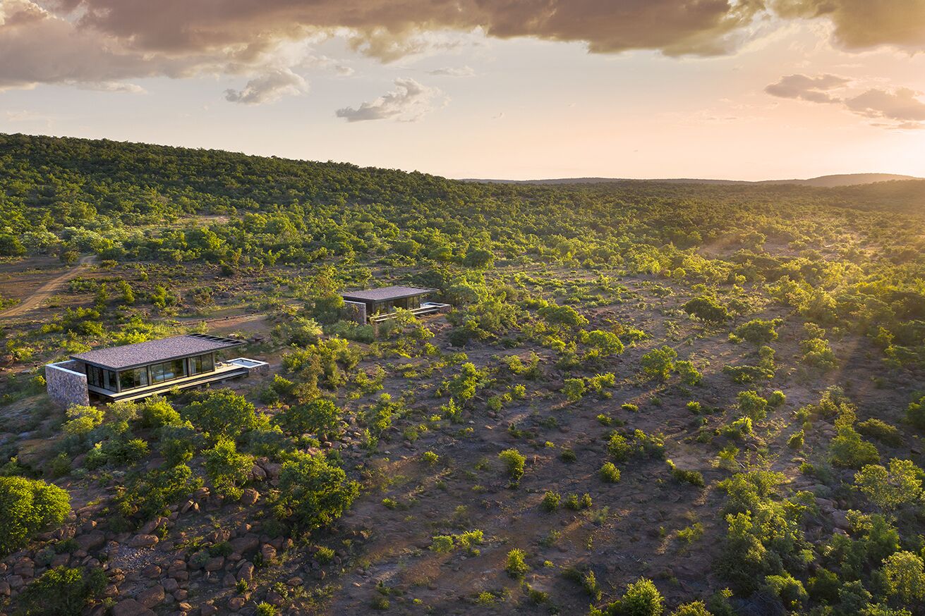 Un edificio moderno de dos pisos con techo plano y amplios ventanales, rodeado de un paisaje verde y exuberante.