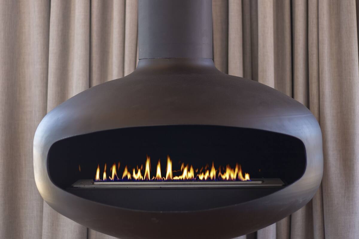 Une cheminée moderne au design épuré, avec un feu visible et des rideaux en arrière-plan.