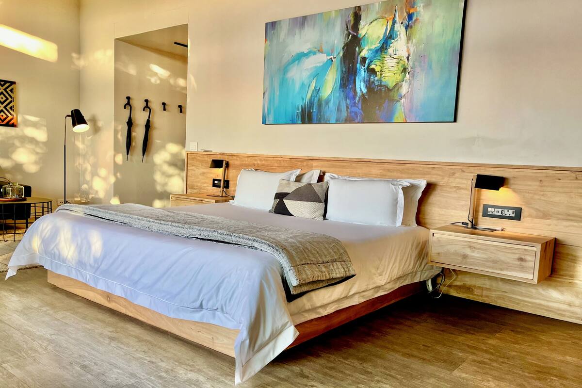 Une chambre à coucher moderne avec un grand lit, une tête de lit en bois, des lampes de chevet et un tableau abstrait aux couleurs vives accroché au mur.