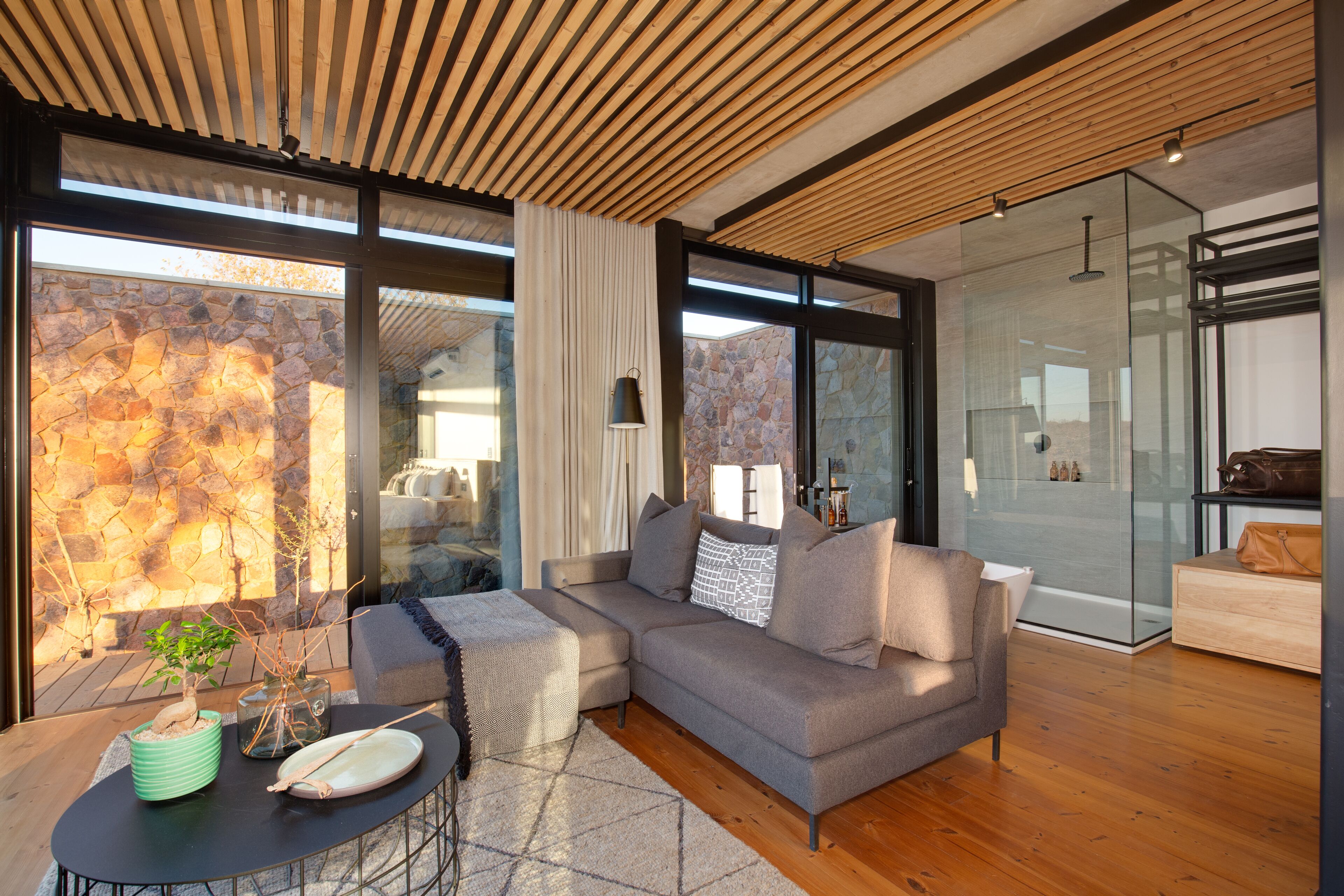 A modern living room with a grey sectional sofa, a round coffee table, and a stone wall.