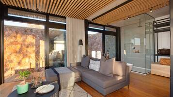 A modern living room with a grey sectional sofa, a round coffee table, and a stone wall.